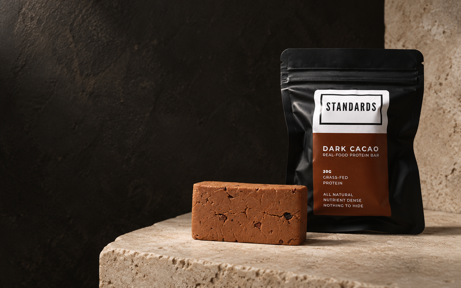 Standards Dark Cacao pouch and an unwrapped protein bar on stone